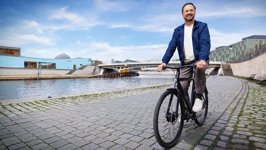 Man sieht Matin vom Bundesministerium des Innern und für Heimat vor einem Fluss auf einem Fahrrad.